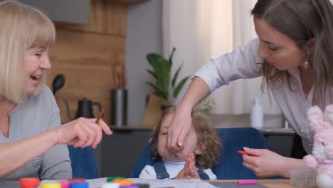 a family moment at home, showing a child, mother, and grandmother engaging in playful interactions and drawing activities
