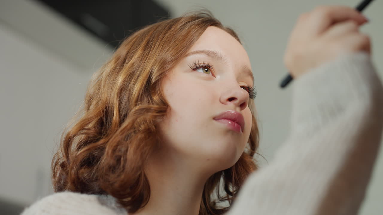 Youthful Makeup Session, Caucasian Adolescent Focused On Makeup Application In Warm Kitchen Setting, Teenager Concentrating On Eyeliner Technique While Wearing Soft Sweater In Kitchen Ambiance