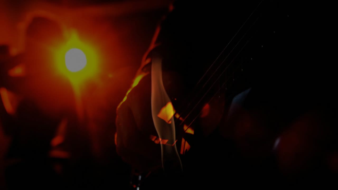Un riflettore arancione che illumina fumo che sale riscaldando le corde della chitarra mentre un musicista strimpella nel microfono.