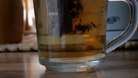 tea bag inside transparent tea cup just filled with hot water while putting down electric ketle in background