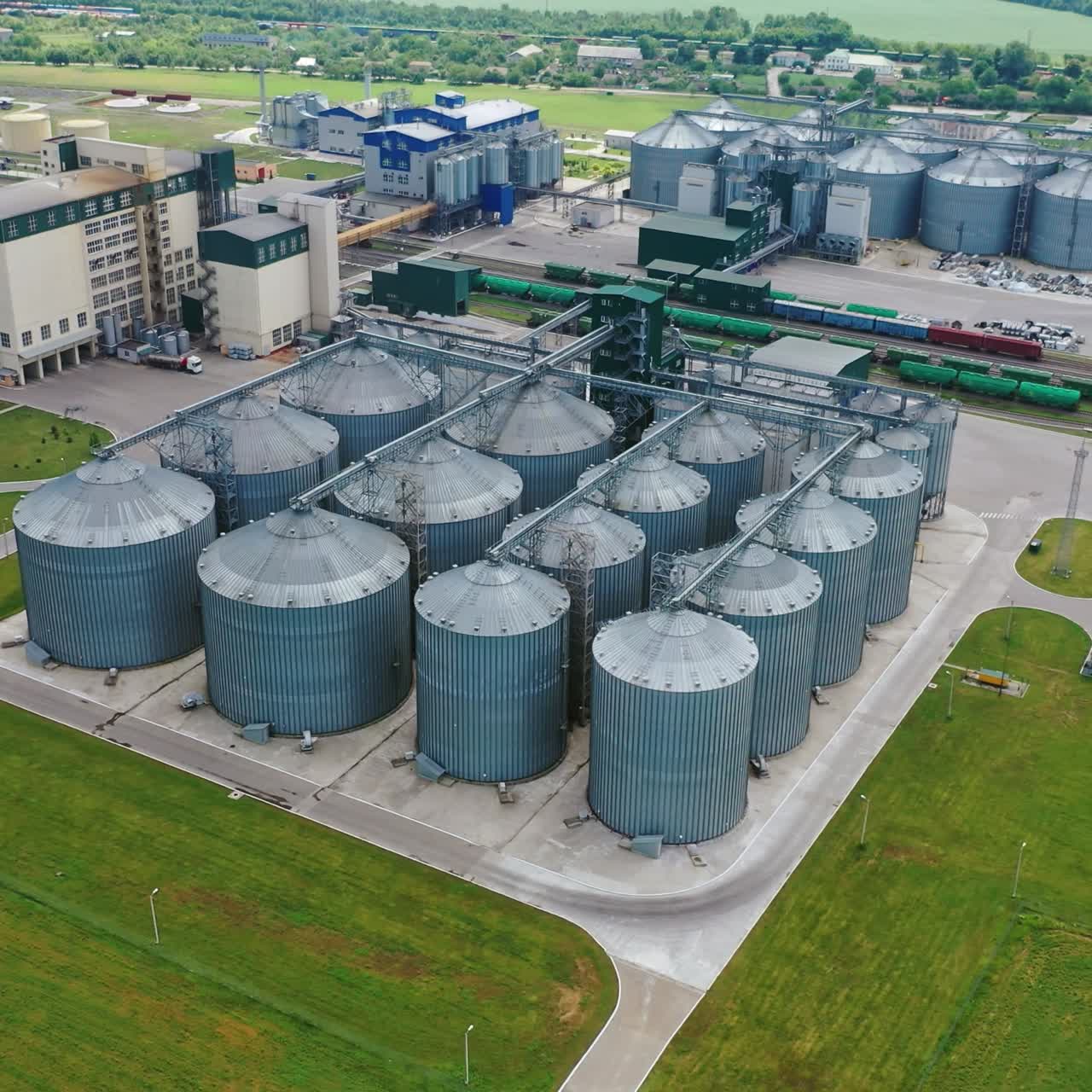 Steel grain terminals in the countryside. Modern granary for keeping agriculture crop on green field. View from the air. Motion camera top down.