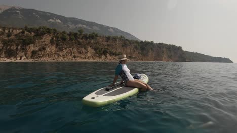 a girl splashing her feet in water as she's resting on a standup paddling board