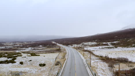 Wintery-Road-Between-Countryside-Fields-With-Misty-Mountain-In-The-Distance-In-Norway