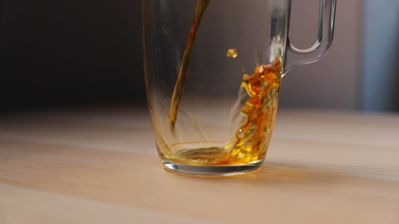 Caffè versato da una caffettiera a stantuffo in vetro con manico in legno in un bicchiere alto, ripreso dal basso in slow motion a 120 FPS.