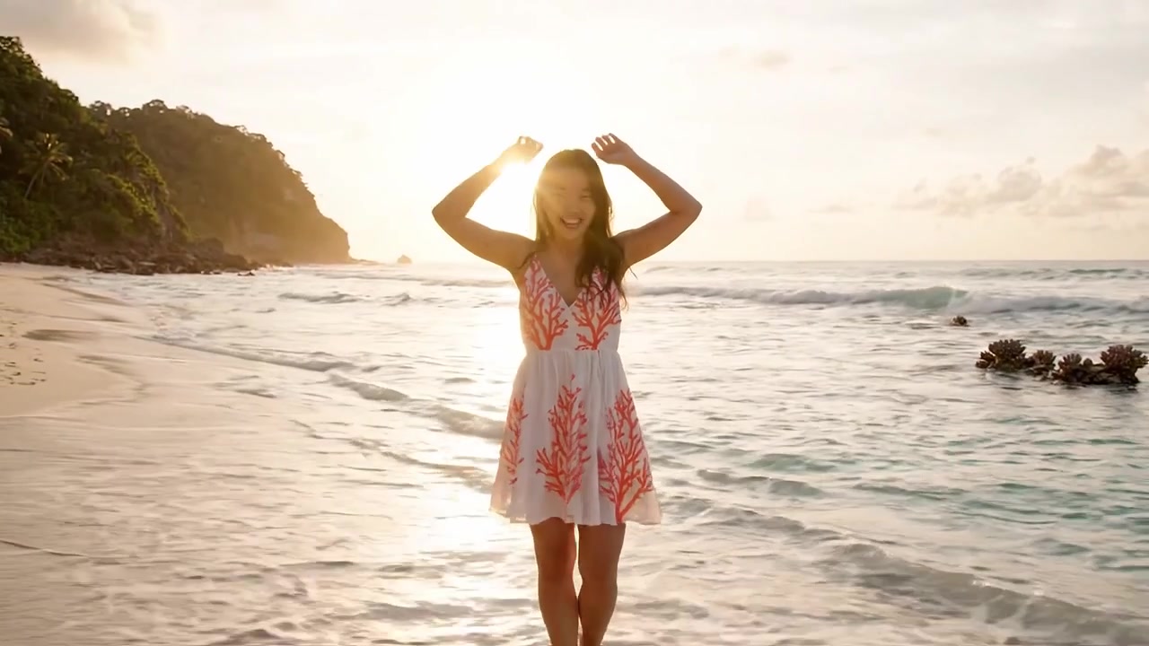 Momento gioioso in spiaggia: una donna in abito svolazzante abbraccia le onde dell'oceano al tramonto, mostrando bellezza e serenità in un paradiso costiero.