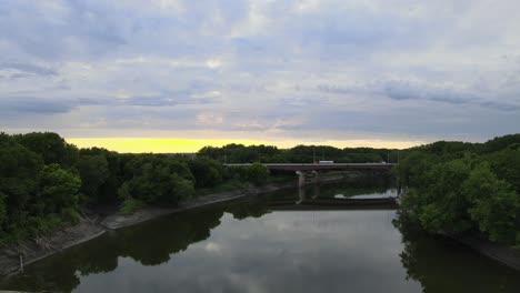 Mientras-Las-Puestas-De-Sol-Sobre-El-Puente-De-La-Carretera-Que-Cruza-Un-Río-Que-Alimenta-El-Mississippi-Al-Sur-De-Las-Ciudades-Gemelas-En-Minnesota,-La-Costa-Se-Refleja-En-Las-Aguas-Tranquilas