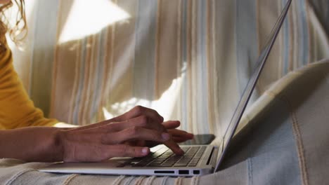 Hands-of-mixed-race-woman-lying-on-couch-using-laptop-in-sunny-living-room