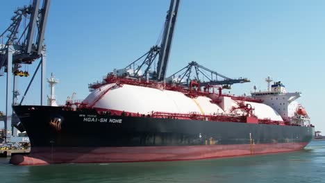 a massive liquefied natural gas carrier maneuvers in port, showcasing industrial might and maritime engineering in favorable weather conditions