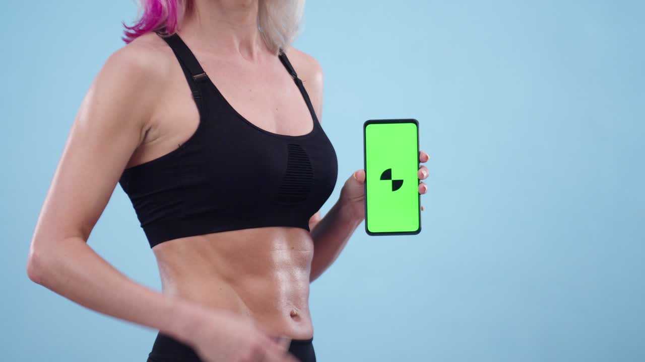 스포츠 을 입고 근육질의 배를 가진 여성은 앱을 가진 전화를 들고, 클로즈업. 스포츠에 대한 앱과 프로그램의 개념