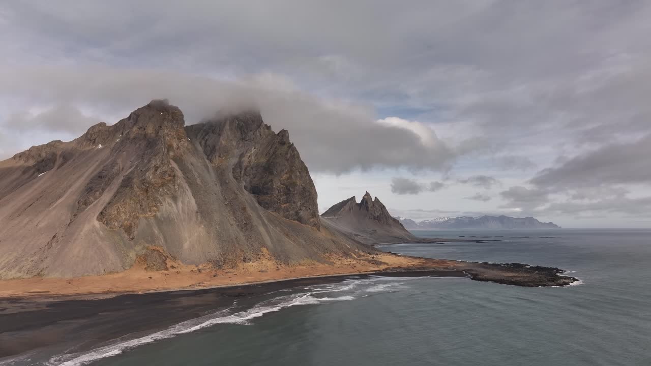Aerial view of The Mountains, Vestrahorn, Eystrahorn, and Brunnhorn, under a cloudy sky along the rugged coast of Stokksnes, Iceland.