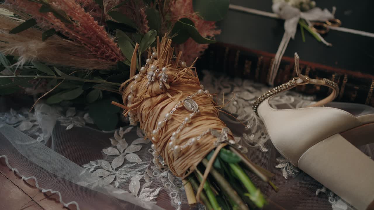 Close up of a rustic wedding bouquet wrapped in raffia with pearls, next to bridal heels