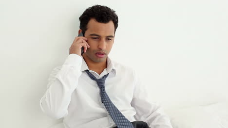 Serious-handsome-businessman-sitting-on-bed-phoning