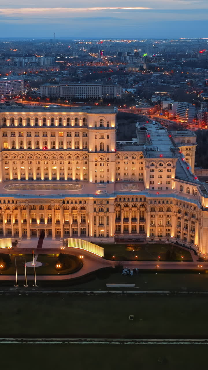 Vertical aerial drone view of illuminated Palace of the Parliament in Bucharest downtown in the evening. Multiple districts around. Romania
