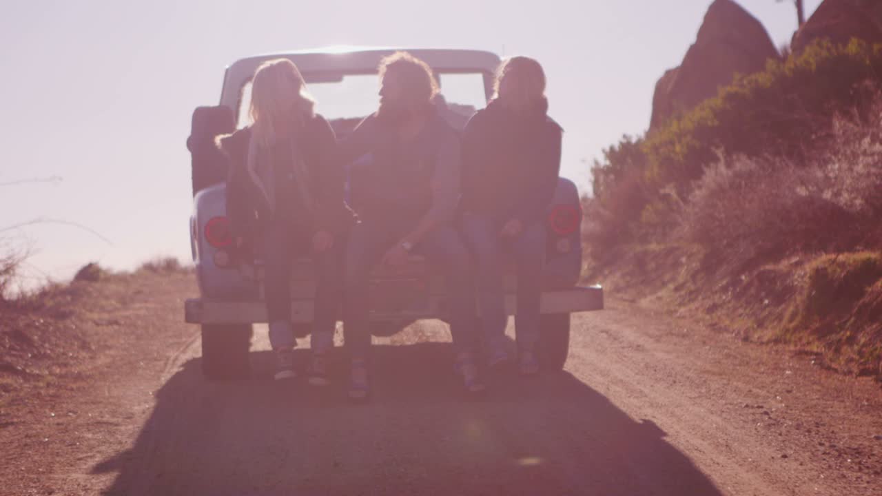 한 무리의 친구들이 시골길을 따라 운전할 때 픽업트럭 뒤에 앉아 있다