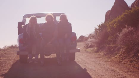 een groep vrienden zit achter in een pick-up terwijl deze over een landelijke weg rijdt