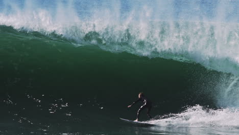 Wave breaks cleanly over surfer riding deep inside steep, green cylindrical barrel