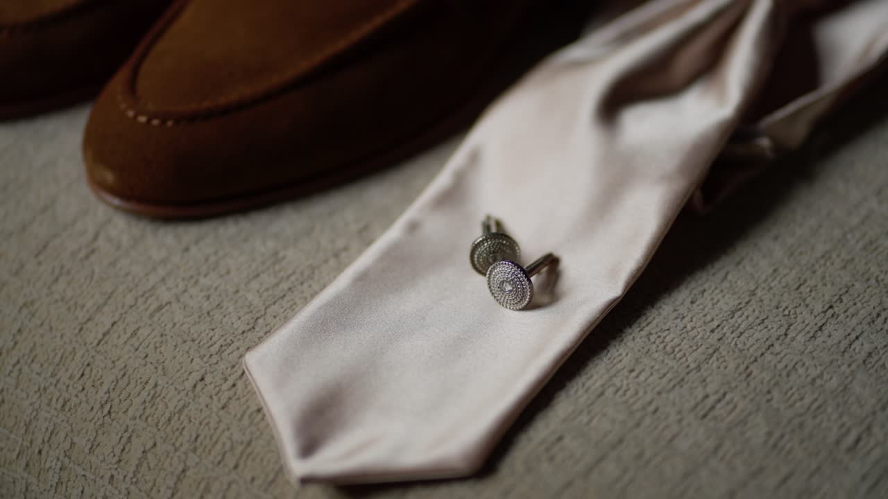 corbata blanca con gemelos de plata colocados en tela texturizada, junto con zapatos formales marrones
