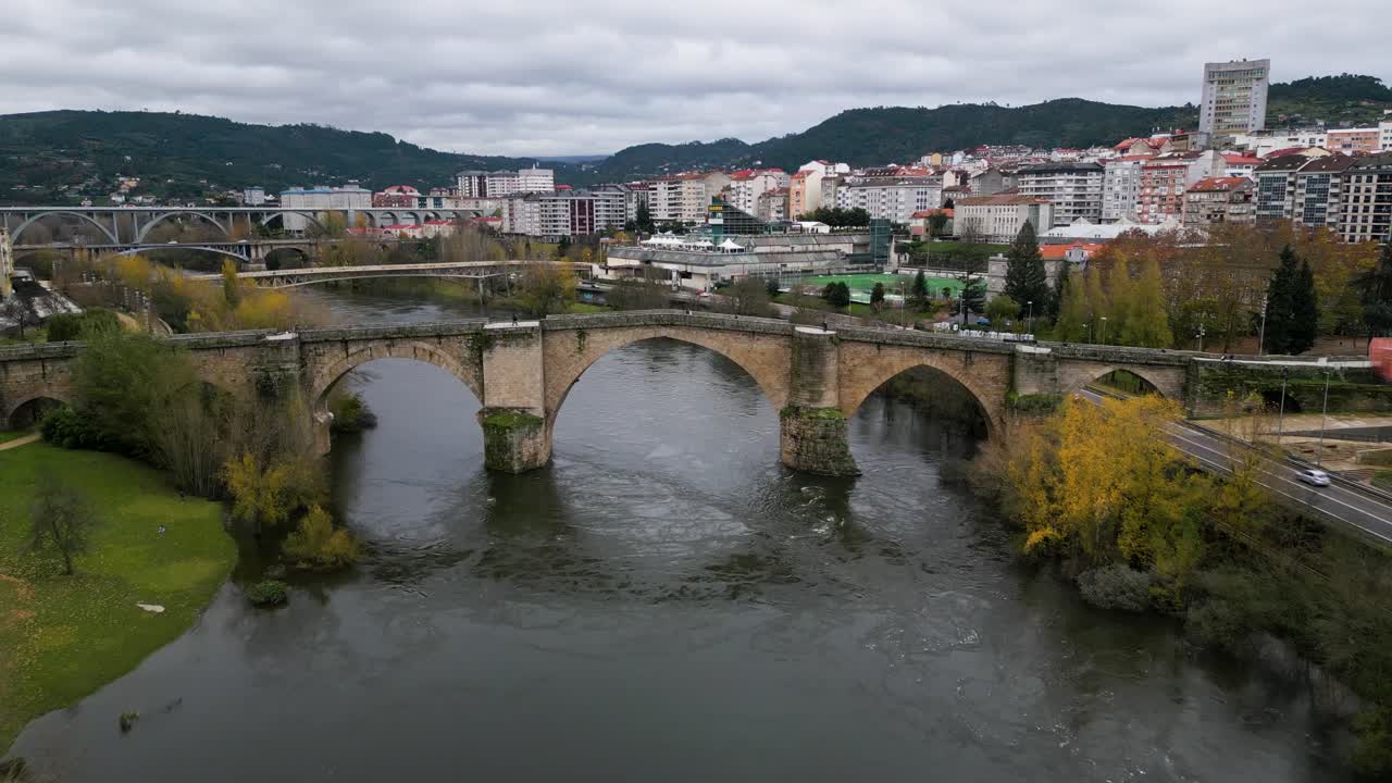 Drone pulls back as tourists walk across Ourense Roman Bridge on Mi&ntilde;o River in Ourense, Galicia, Spain