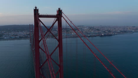 Aerial-orbit-of-large-red-Ponte-25-de-Abril-bridge-with-car-traffic-crossing-the-sea-on-the-coast-of-Lisbon,-Portugal