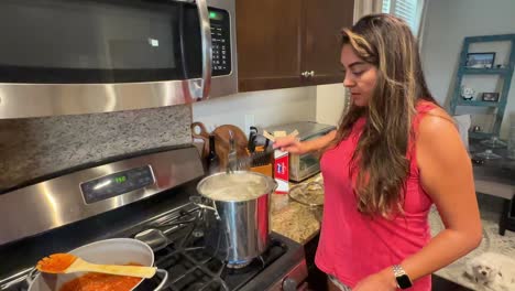 hispanic woman in kitchen cooking, stirring pasta and homemade sauce over a hot stove