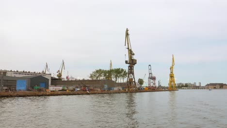 sailing past the industrial seaport with huge cranes and depots in the city of gdansk.