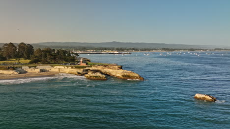 Santa-Cruz-California-Aerial-v1-fly-around-lighthouse-point-and-seal-rock-with-waves-crashing-on-the-shore,-panning-view-reveals-glowing-sun-in-the-sky-at-sunset---Shot-with-Mavic-3-Cine---May-2022