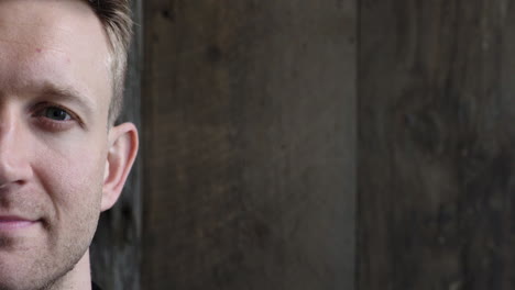 half-face-close-up-portrait-of-young-attractive-blonde-man-looking-calm-at-camera-pensive-caucasian-male--on-wooden-background-copy-space