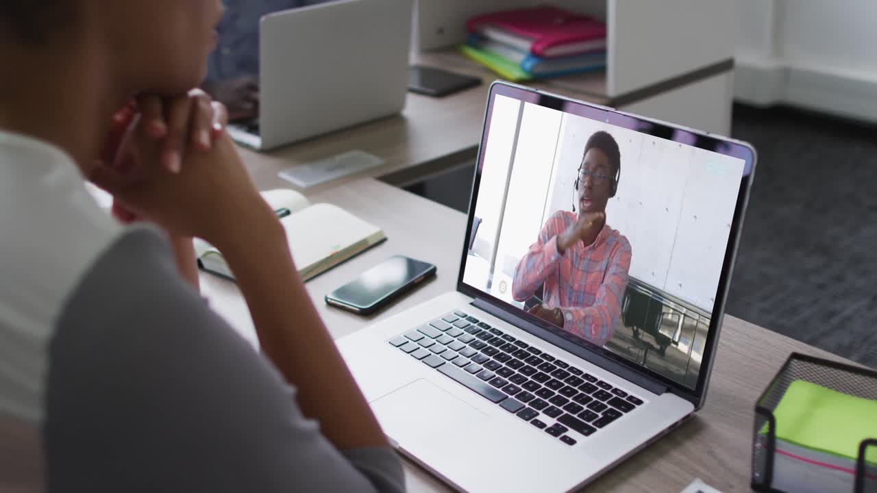 mujer afroamericana teniendo una videoconferencia en una computadora portátil con un colega de oficina masculino en la oficina