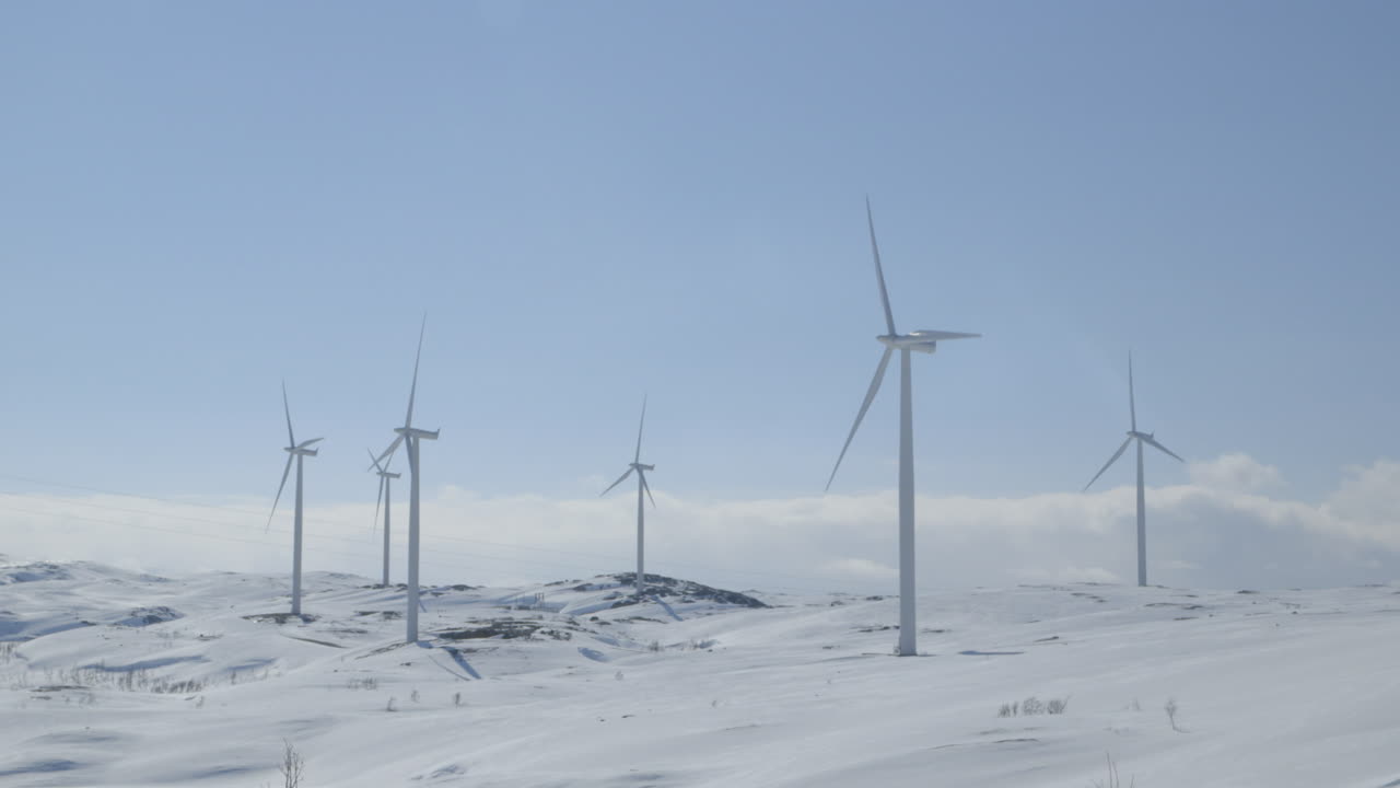 Cinematic leftward pan across snow-dusted wind turbines in bright alpine light. Focused on windmill energy independence, climate action, and rural power solutions.