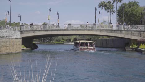 a passenger boat travels underneath a busy bridge full of people