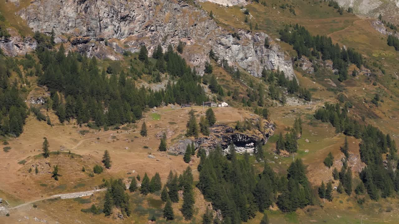 Aerial panning right revealing an isolated rock cabin in a pine forest in Italy, Aosta Valley, Valle d’Aosta, surrounded by alpine mountains