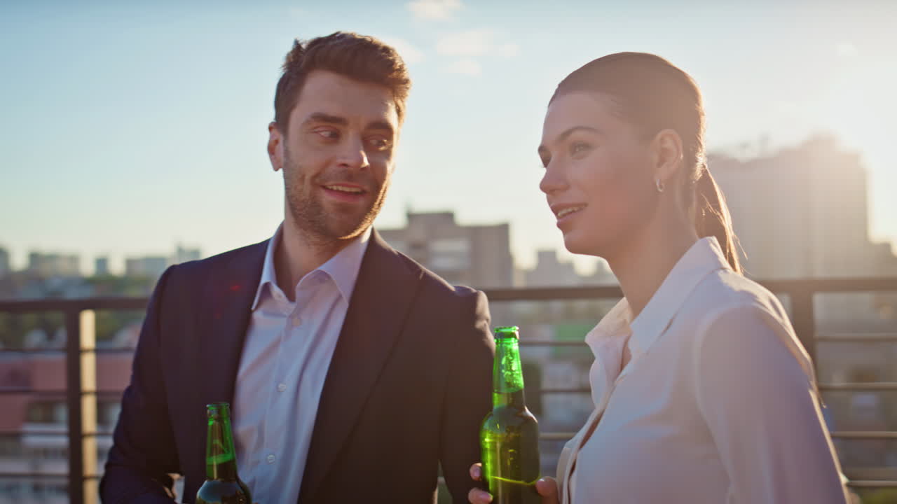Primer plano de amigos sujetando botellas de cerveza en una azotea al atardecer. Compañeros felices hablando.