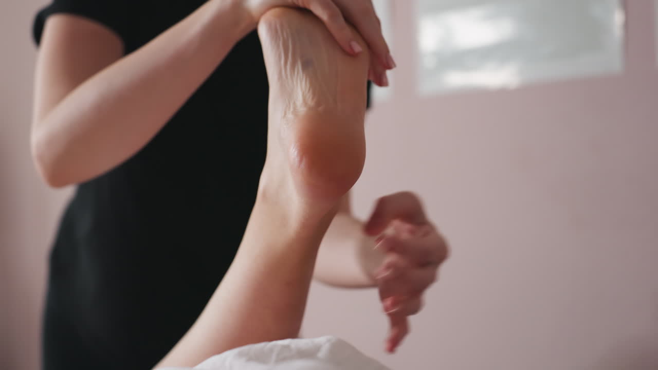 Close view of massage therapist gently holding client's bare foot during soothing foot massage therapy session in calming room, focusing on relaxation, muscle relief, and professional body care