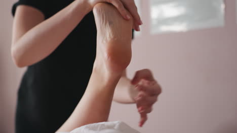 close view of massage therapist gently holding client's bare foot during soothing foot massage therapy session in calming room, focusing on relaxation, muscle relief, and professional body care