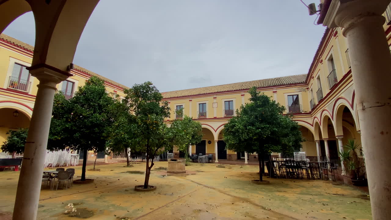 Un tranquillo cortile appartato con archi, alberi di arancio e sedie vuote, luce soffusa dopo la tempesta in un antico edificio andaluso