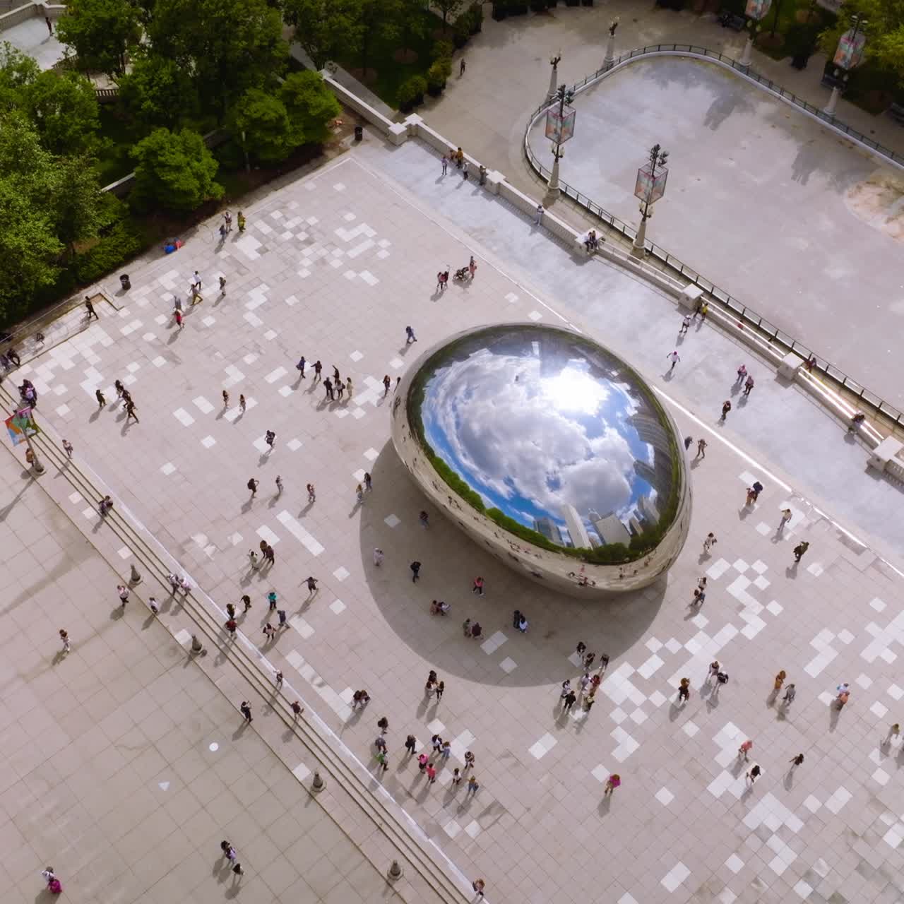 Iconic Cloud Gate surrounded by numerous tourists visiting the site. Top view on the blue cloudy sky reflecting in the big shining Bean