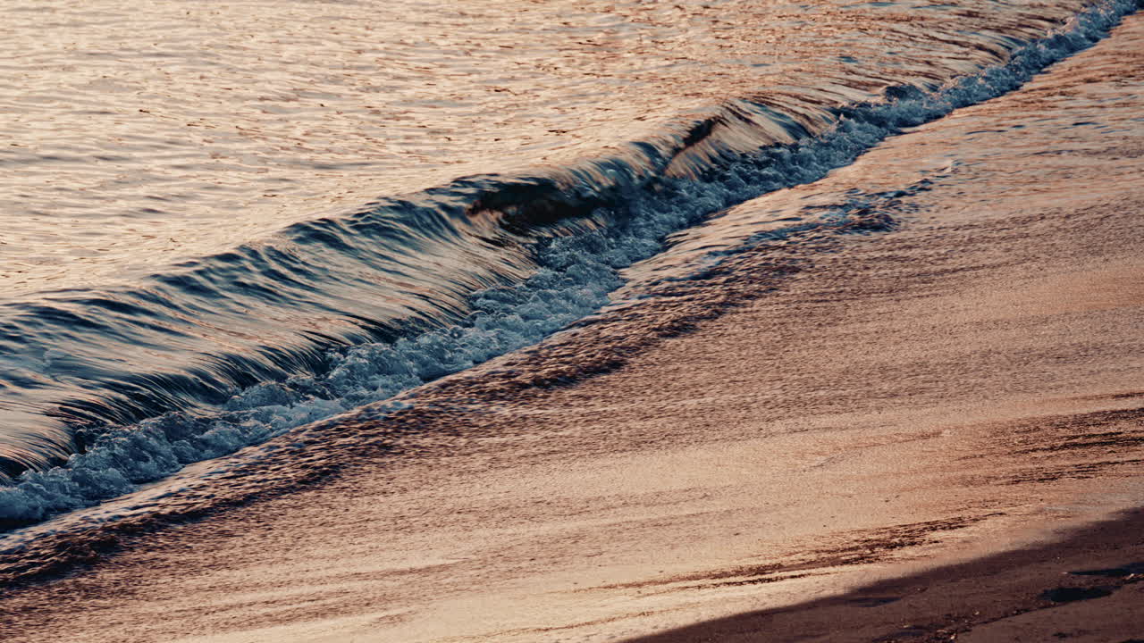 Onde marine delicate che si infrangono su una spiaggia sabbiosa durante il tramonto, con barche a vela ancorate visibili all'orizzonte