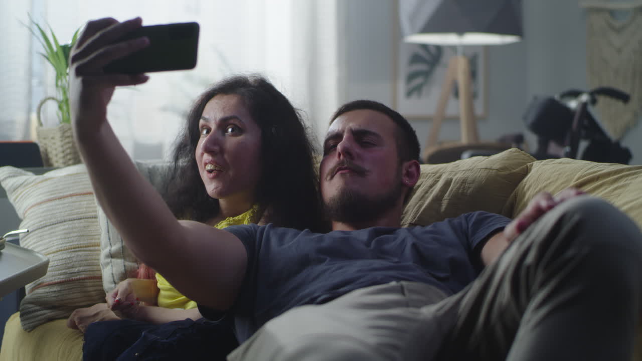woman with a Disability and Man Taking Selfie Woman with a Physical Disability and Man Laughing and Taking a Selfie together on Smartphone for Social Networks Sitting on a Couch at Home