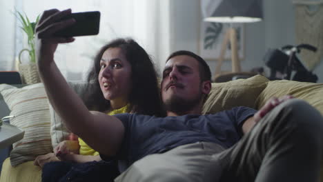 woman with a disability and man taking selfie woman with a physical disability and man laughing and taking a selfie together on smartphone for social networks sitting on a couch at home