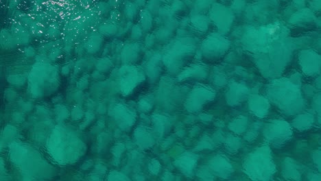 aerial tilts up above clean sea water revealing stones, natural landscape with sunshine reflection