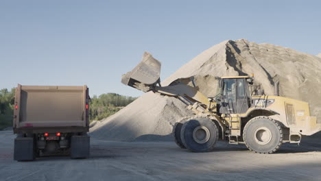 daylight quarry operations with front loader unloading sand into dump truck container