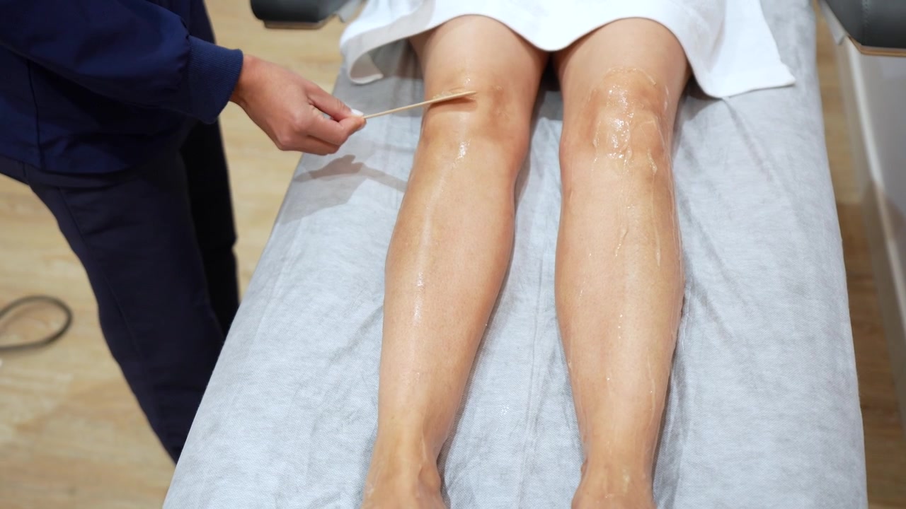 Estetista che applica il gel sulle gambe della cliente per un trattamento di epilazione laser