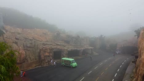 Toma-Aérea-Ascendente-De-Un-Vehículo-De-Autocar-Verde-Y-Turistas-En-Condiciones-De-Niebla-Y-Malas-Condiciones-Climáticas-Lluviosas