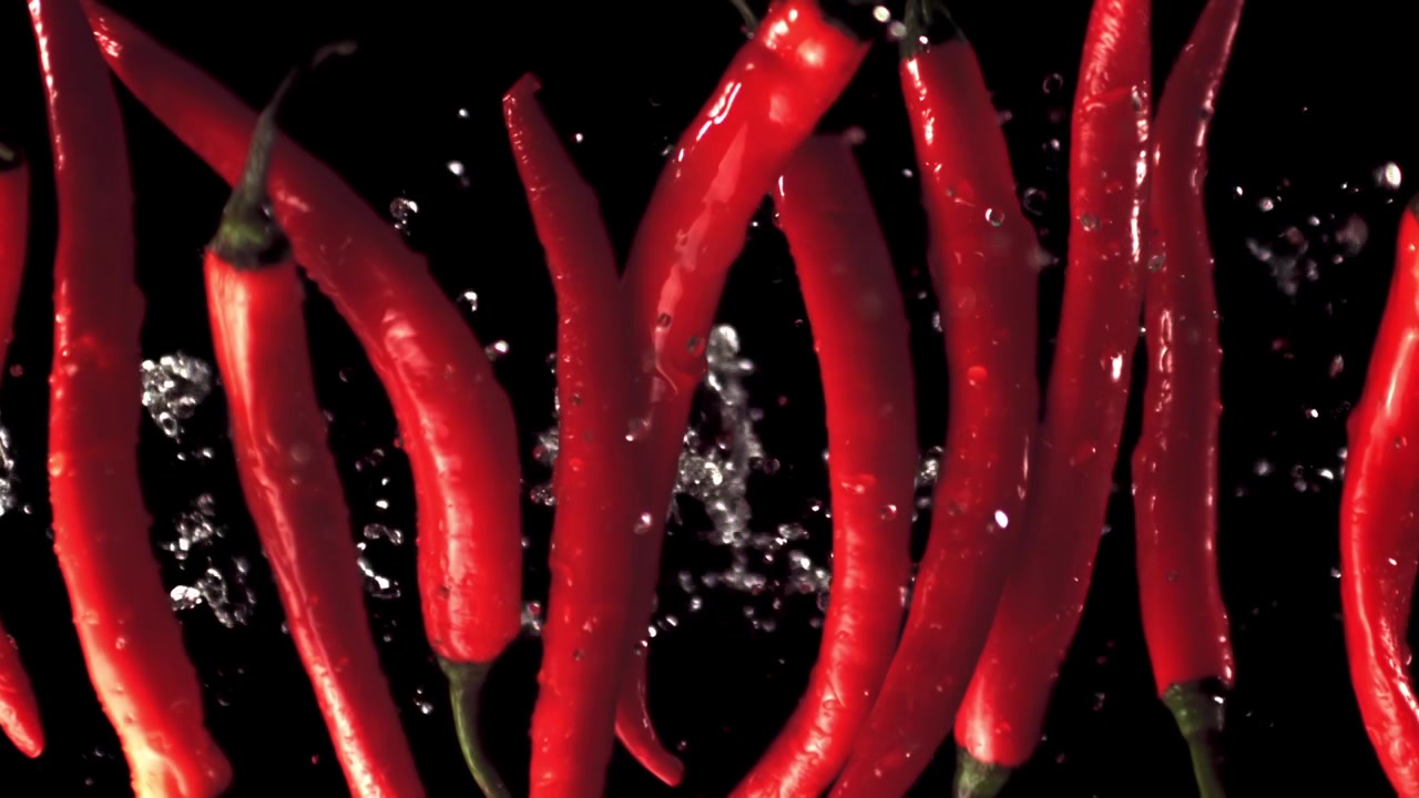 Red Chili Peppers with Splashing Water on Black Background in Slow Motion