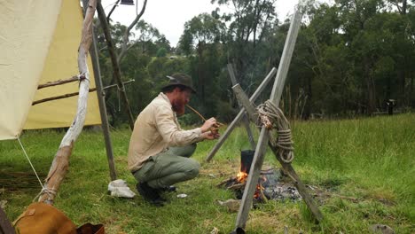 un bosquero australiano en su campamento histórico enciende una pipa de tabaco junto a una fogata en el bosque
