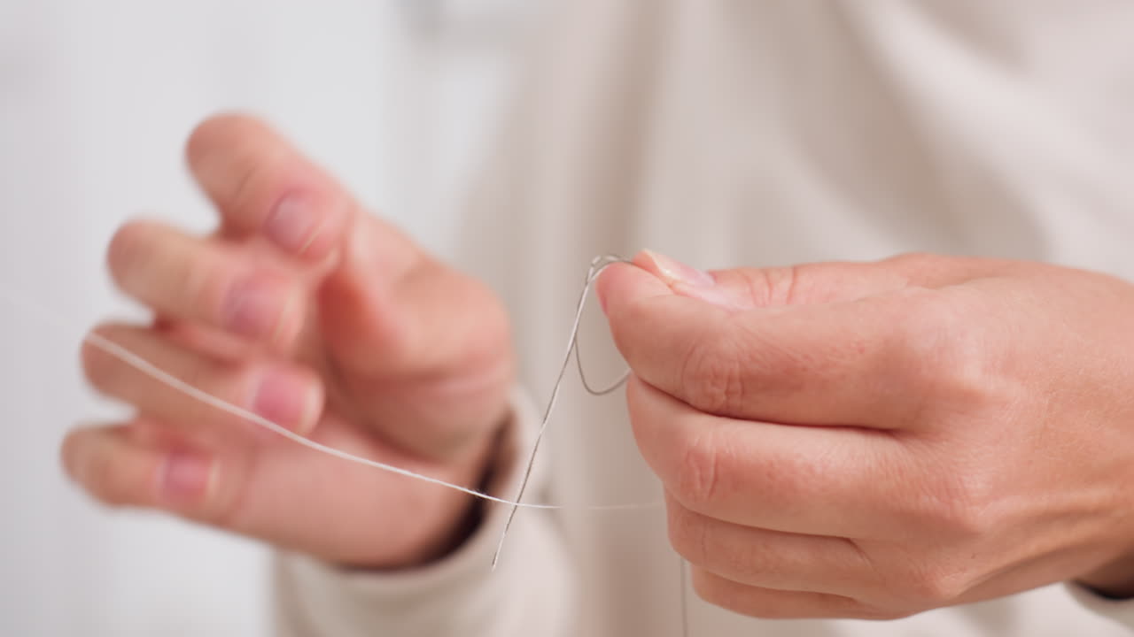 Female hands carefully tying two strings, displaying focus, skill, close detail, and delicate technique in minimal sewing environment, highlighting manual precision and calm approach to craft