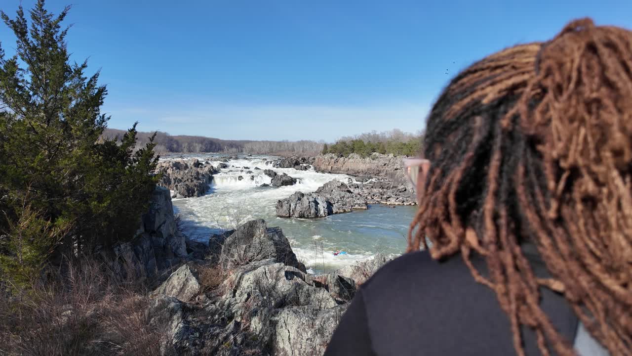 Woman looking at the rocky river rapids and waterfalls on a sunny day