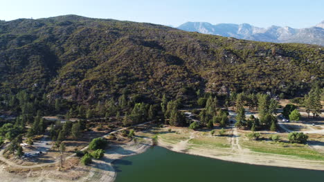 Mountain-covered-in-dense-forest-near-coastline-of-lake-Hemet,-aerial-view