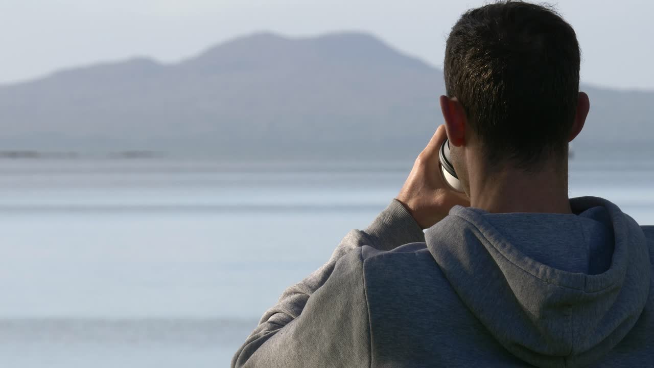 뉴질랜드 오클랜드의 해변 벤치에 앉아 커피를 마시는 백인 남자의 뒷모습