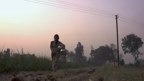 indian woman walking in sunset with water buckets